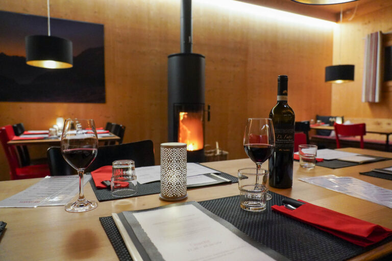 Am Tisch im Restaurant Aratsch mit einem Glas Rotwein aus unserer hervorragenden Auswahl und Cheminée-Feuer