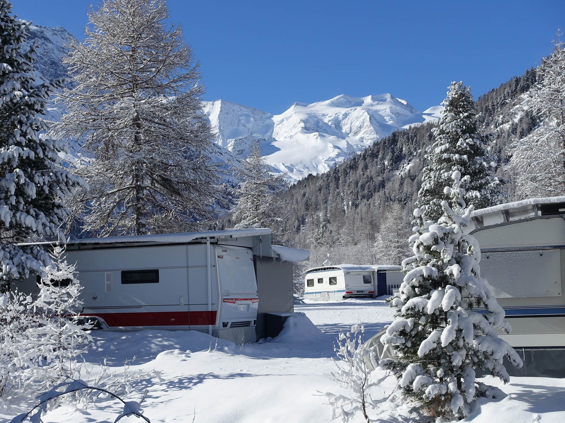 Wohnmobil-Stellplätze im Winter mit Aussicht auf die verschneiten Alpen beim Camping Morteratsch