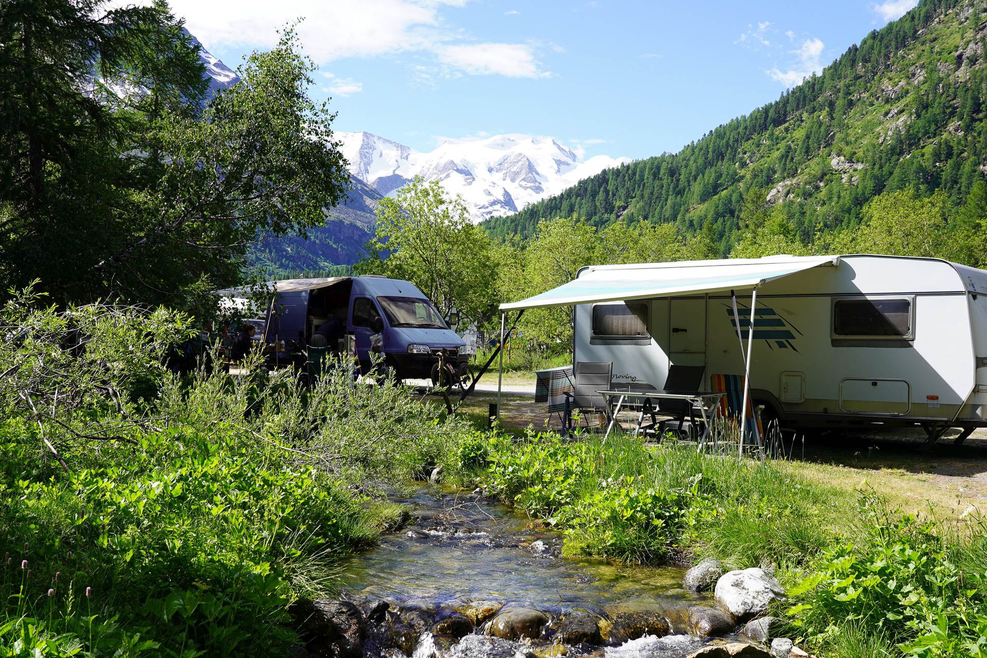 Standplatz für Wohnwagen und Kastenwagen am Bach mit den Berggipfeln im Hintergrund